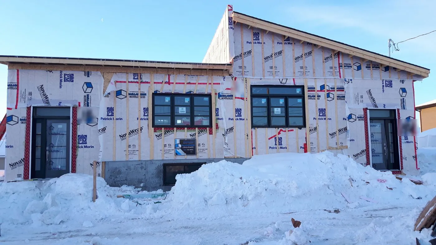 Duplex en chantier en hiver : portes et fenêtres posées, murs fermés par la membrane pare-air