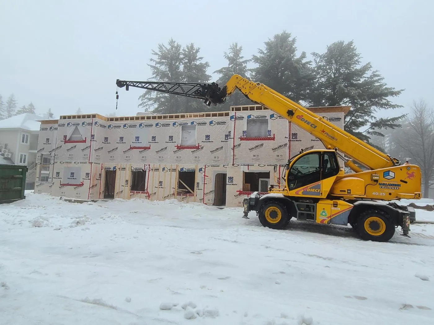 Immeuble multi-logements fermé par sa membrane pare-air sous la neige, chariot télescopique au premier plan
