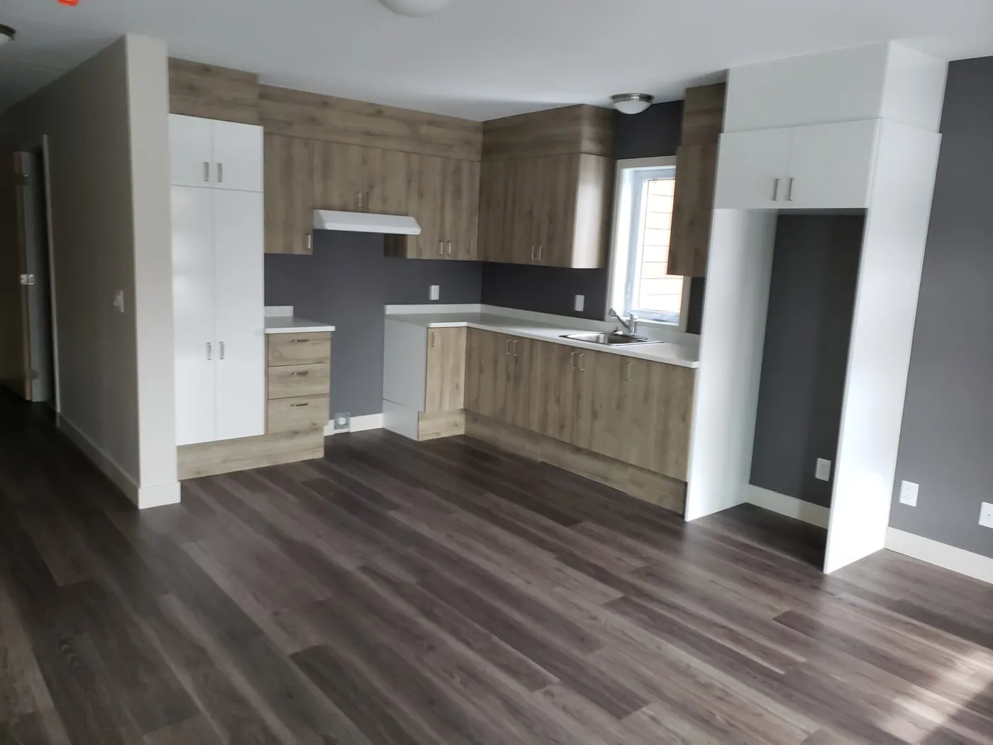 Cuisine installée dans une maison neuve : armoires de bois, comptoir blanc et plancher posés