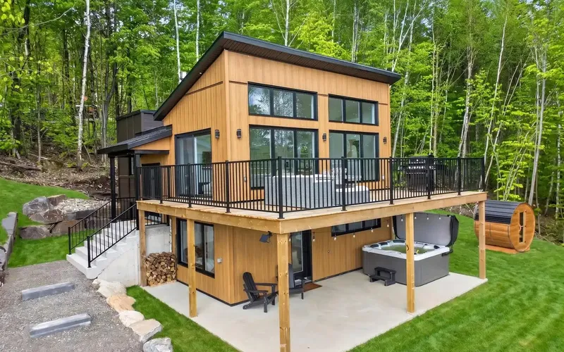 Façade du chalet en bardage de bois vertical avec terrasse sur poteaux et bain tourbillon