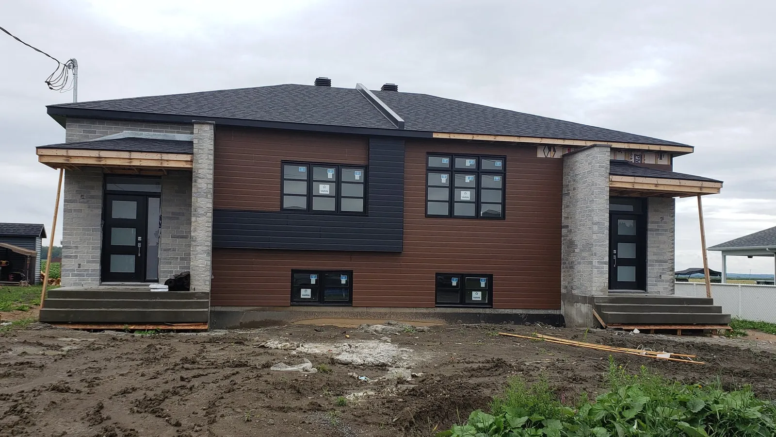 Façade avant en fin de chantier : parement posé, soffites encore à finir et terrain toujours en terre