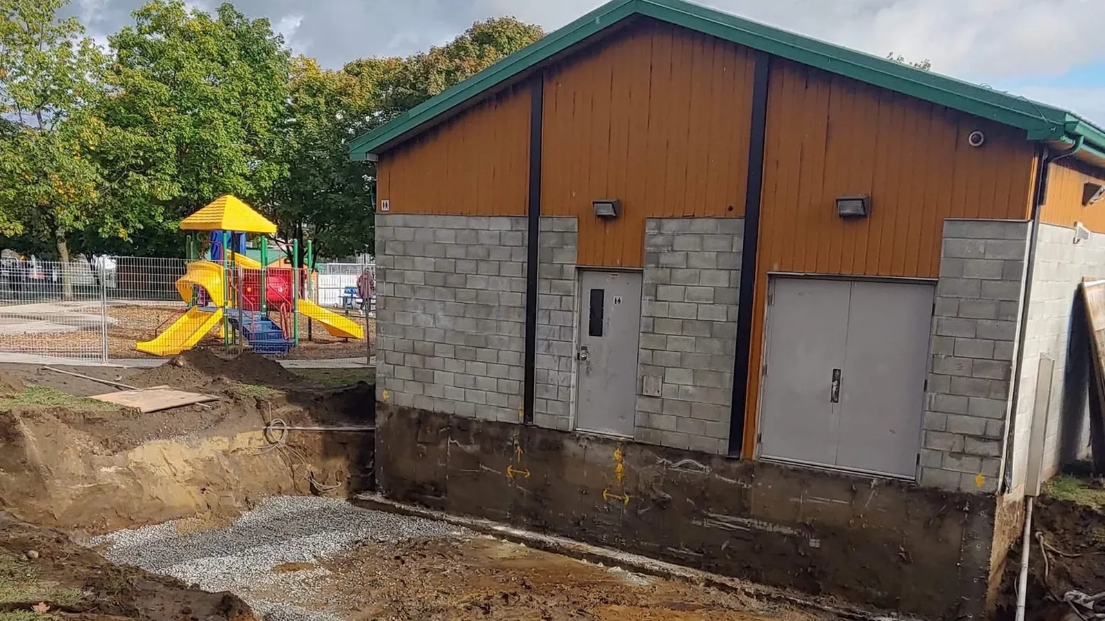 Tranchée ouverte le long de la fondation du bâtiment existant, avec son parement de bois et sa toiture d’origine