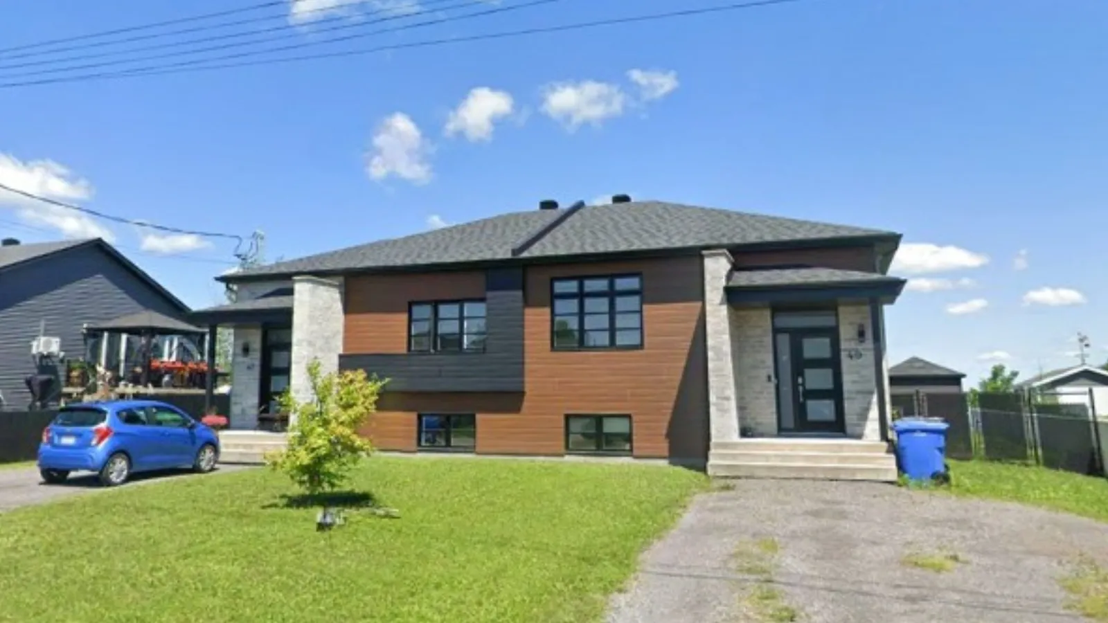 Façade avant du duplex : parement de bois brun, panneaux gris foncé, brique blanche et encadrements de fenêtres noirs